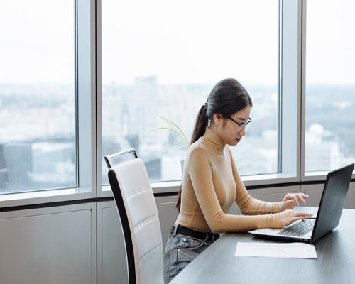 A person typing calmly on a laptop near a bright window