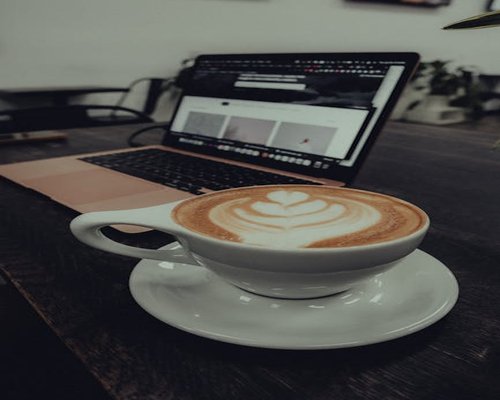 A warm cup of coffee and a laptop on a wooden table, representing digital browsing